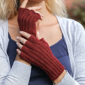 Könnte beinhalten: Ein Paar fingerlose Handschuhe in Burgunderrot aus gestrickter Wolle. Die Handschuhe haben eine gerippte Struktur und werden von einer Person getragen.