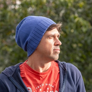 May include: A solid blue knit beanie with a ribbed cuff edge. The beanie is made of a soft, flexible material that fits snugly around the head, featuring a consistent, smooth texture throughout the main body and a distinct ribbed pattern at the base.