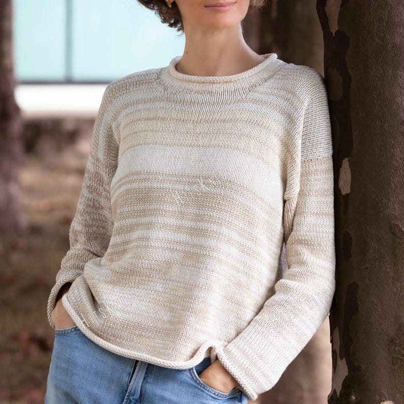 May include: A long-sleeved knit sweater featuring a horizontal striped pattern in shades of cream, beige, and white. The garment has a round neckline, raglan sleeves, and a straight hemline, constructed with a medium-weight yarn texture.