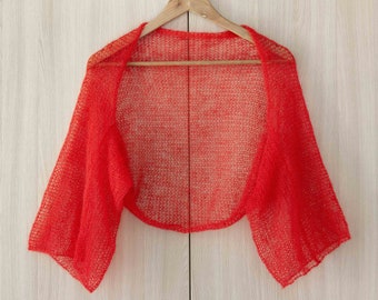 May include: A red knitted shrug with a delicate open weave pattern. The shrug has a short, cropped length and three-quarter sleeves.