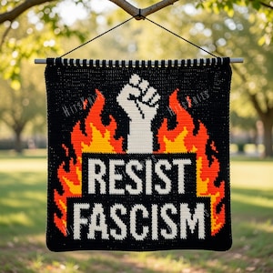 May include: Black banner with the words "RESIST FASCISM" in white block letters. A white fist is above the text, with flames in orange and yellow. The banner is hanging from a tree branch.