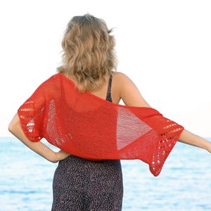 K&ouml;nnte beinhalten: Ein leuchtend roter Strick-Shrug mit einem durchbrochenen Strickmuster an den R&auml;ndern und einer leichten, halbtransparenten Textur. Das Kleidungsst&uuml;ck liegt &uuml;ber den Schultern und dem oberen R&uuml;cken und zeigt ein gleichm&auml;&szlig;iges Strickbild.