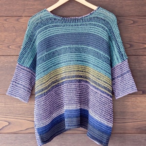 May include: A striped knit sweater with a loose fit and a wide neckline. The sweater is made in a variety of shades of blue, green, and purple.