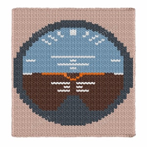May include: A knitted square featuring a stylized airplane instrument panel design. The panel is primarily blue, brown, and white, with a light tan border. The design includes various indicators and markings, creating a textured, handcrafted appearance.