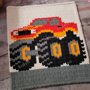 May include: A handmade, square, crocheted blanket featuring a pixelated monster truck design. The truck is red, orange, yellow, gray, and black, with the word "COO" on the tire. The blanket has a white top, gray bottom, and the text "HitsKnits".