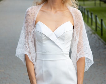 May include: A white knit shrug with a delicate open weave pattern. The shrug has a loose fit and is perfect for layering over a dress or top.