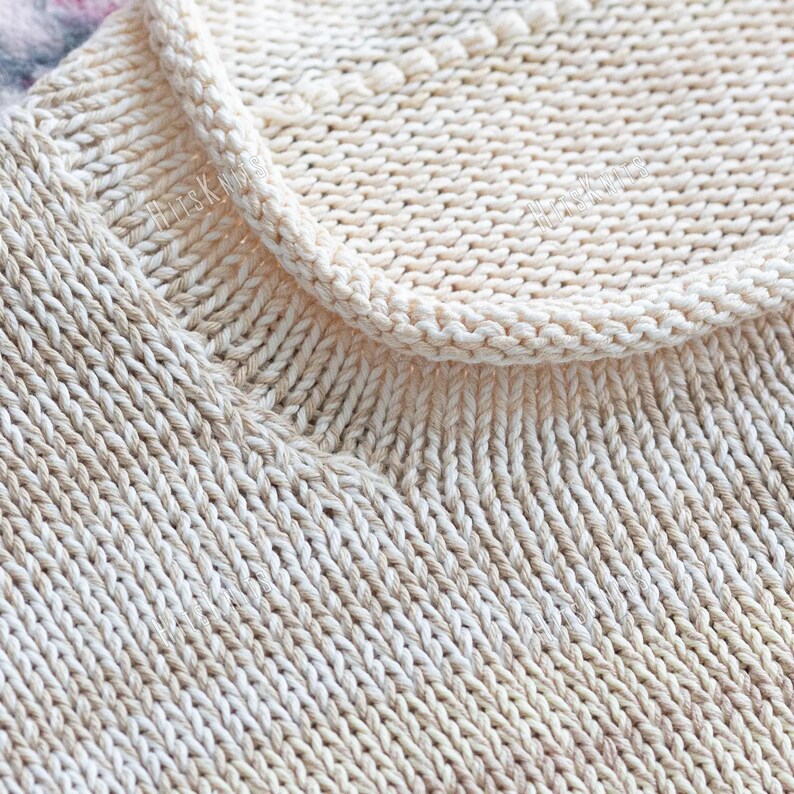 May include: A cream-colored knitted garment featuring a ribbed neckline and a textured stitch pattern. The fabric displays a consistent stockinette stitch throughout the body, with a visible watermark reading HitsKnits across the upper section.