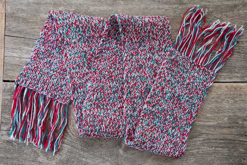 May include: A red, white, and green knitted scarf with fringe on both ends.