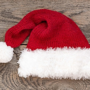 May include: A red knitted Santa hat with a white faux fur trim. The hat has a pom-pom on top.