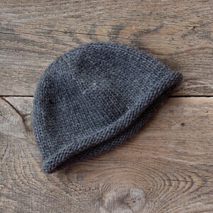 May include: A gray knitted beanie hat on a wooden surface.