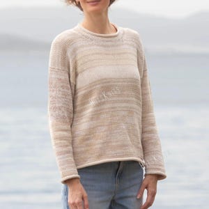 May include: A long-sleeve knit sweater featuring a horizontal striped pattern in shades of beige, cream, and white. The garment has a round neckline and a relaxed fit with a rolled hem. The text HITS KNITS is visible on the front of the sweater.
