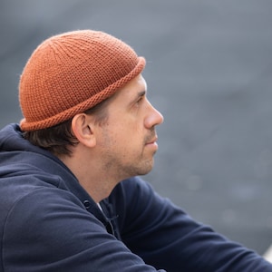 May include: A person wearing a brown knitted beanie with a folded brim. The beanie is made of a soft, textured yarn.