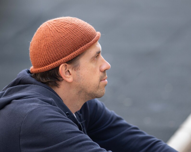 May include: A person wearing a brown knitted beanie with a folded brim. The beanie is made of a soft, textured yarn.