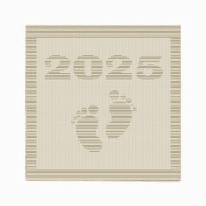 Può includere: Una coperta beige lavorata a maglia con l'anno "2025" e due impronte di piedi di bambino. La coperta ha un bordo a righe ed è realizzata in un materiale morbido e strutturato. Il design è in una tonalità beige più chiara.