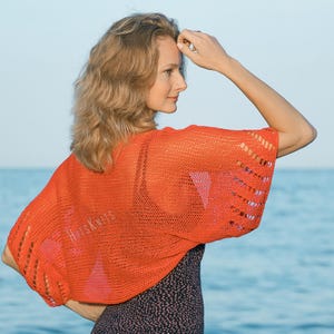 K&ouml;nnte beinhalten: Ein leuchtend orangefarbener H&auml;kel-Bolero mit einem feinen Netzstrickmuster und breiteren, durchbrochenen vertikalen Streifen an den &Auml;rmeln. Das Kleidungsst&uuml;ck hat eine kurze, lockere Passform mit weiten &Auml;rmeln und tr&auml;gt den Text HitsKnits.