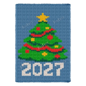 May include: A rectangular blue knitted fabric panel featuring a green Christmas tree design with a yellow star on top, red garland, and yellow ornaments. The white knitted text 2027 is positioned below the tree on the blue background.