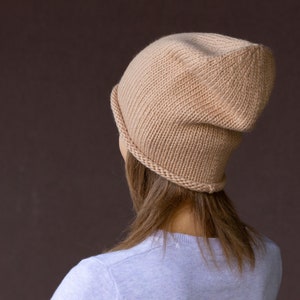 Könnte beinhalten: Eine beige Strickmütze mit einem lässigen Sitz. Die Mütze ist aus einem weichen, warmen Material gefertigt und perfekt, um den Kopf im Winter warm zu halten.
