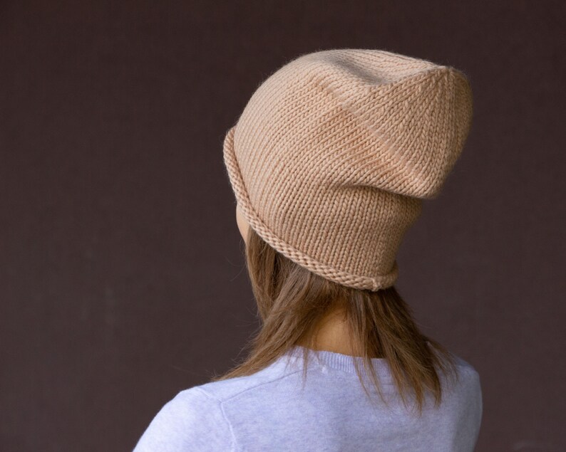 May include: A beige knitted beanie hat with a slouchy fit. The hat is made of a soft, warm material and is perfect for keeping your head warm in the winter.