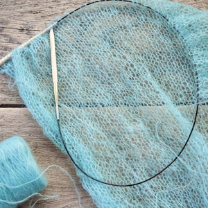 May include: A light blue yarn skein and a partially knitted scarf with two knitting needles. The scarf is made of a delicate, openwork stitch.