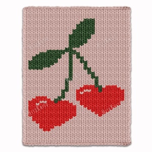 May include: A knitted rectangular item with a pixelated design of two red cherries and green leaves on a light pink background. The cherries are heart-shaped. The item has a textured appearance.