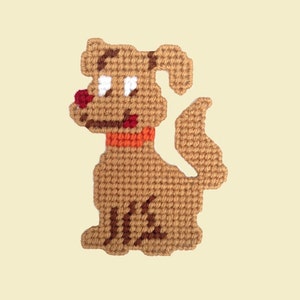 Peut inclure: Un chien en crochet marron avec un collier orange et des yeux blancs. Le chien est assis avec sa queue enroulée derrière lui.