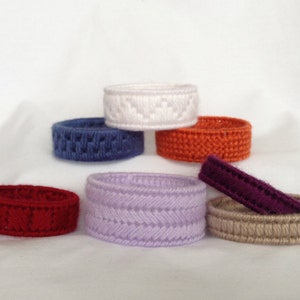 May include: Six crocheted rings in various colors, including white, blue, orange, purple, lavender, and beige. The rings are stacked on top of each other.