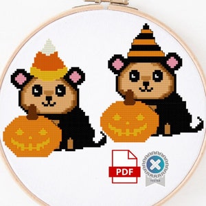 May include: Cross stitch pattern featuring two adorable black and brown bears wearing Halloween costumes. One bear is wearing a candy corn hat and the other is wearing a witch's hat. Both bears are holding a jack-o-lantern pumpkin. The pattern is in PDF format.