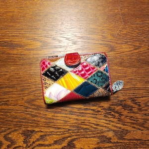 Peut inclure: Un portefeuille rectangulaire présentant un motif patchwork multicolore avec diverses textures, notamment des motifs crocodile gaufrés, des surfaces lisses et des imprimés floraux. Il possède une fermeture à pression rouge et une tirette argentée.