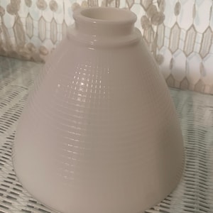 Peut inclure: Abat-jour blanc en forme de cône avec un motif texturé en forme de grille. L'abat-jour a une base arrondie et un sommet cylindrique. L'arrière-plan comprend une surface en osier blanc et un rideau à motifs.
