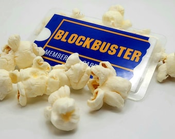 May include: A blue and yellow Blockbuster membership card with the text "Blockbuster Member Card" on it, surrounded by white popcorn kernels.