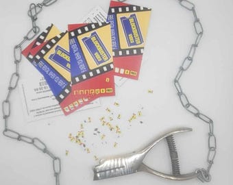 May include: A silver chain, a silver hole punch, and four red and blue Blockbuster Video rental cards with the text "FREE RENTAL WHEN YOU RENT 6" on them. The cards are scattered on a white surface with small pieces of paper.