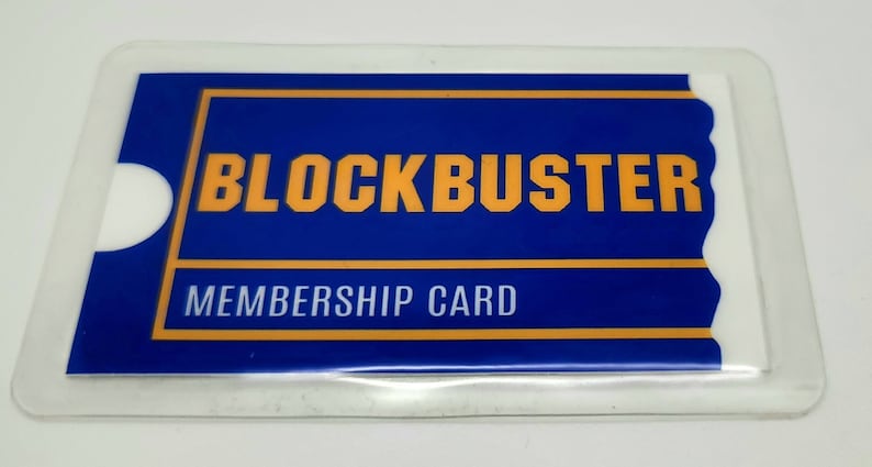 May include: A rectangular Blockbuster membership card encased in a clear plastic protective sleeve. The card features a blue background with the word BLOCKBUSTER printed in bold yellow letters, and the text MEMBERSHIP CARD in white below.