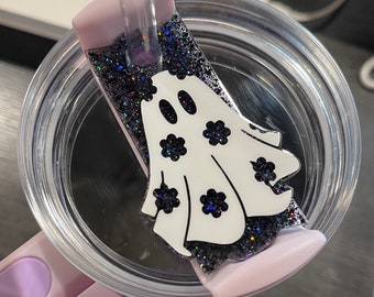 May include: A white ghost with black flower accents on a black glitter background. The ghost is attached to a pink and clear tumbler lid.