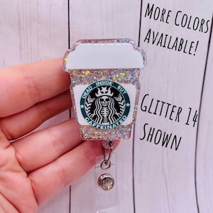 May include: A clear glitter coffee cup with a black and green skull and crossbones design. The text on the cup reads "Dead Inside But Caffeinated". The cup is attached to a clear retractable badge holder.