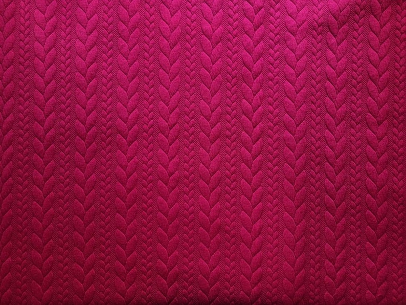 Peut inclure: Gros plan sur un tissu magenta fonc&eacute;. Le tissu pr&eacute;sente un motif en relief r&eacute;p&eacute;t&eacute;, semblable &agrave; des tresses, cr&eacute;ant un effet tridimensionnel. La texture est riche et visuellement attrayante, avec une couleur magenta profonde.