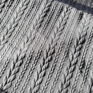 Peut inclure: Gros plan sur un tissu gris avec un motif r&eacute;p&eacute;t&eacute; de motifs en relief en forme de feuilles. La texture est d&eacute;taill&eacute;e, avec les feuilles dispos&eacute;es en diagonale. Le tissu semble doux et textur&eacute;.