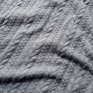 Peut inclure: Gros plan sur un tissu gris avec un motif de feuilles en relief. La texture cr&eacute;e un motif r&eacute;p&eacute;titif sur le mat&eacute;riau. Le tissu semble doux et souple, avec des plis et des ombres d&eacute;licats.