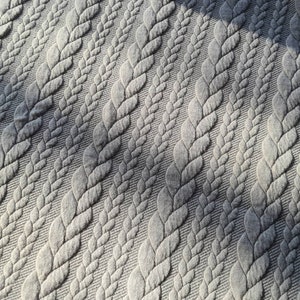 Peut inclure: Gros plan sur un tissu gris avec un motif r&eacute;p&eacute;t&eacute; de motifs tress&eacute;s en relief. La texture cr&eacute;e une sensation de profondeur et de dimension, les ombres accentuant l'aspect tiss&eacute;. La couleur du tissu est un gris neutre.
