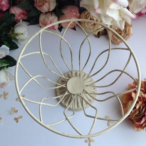 May include: A white metal bowl with a decorative, openwork design. The bowl has a round base and a wide, circular rim.
