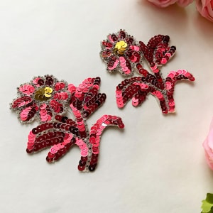 May include: Two pink and red sequined flower appliques with gold centres. The appliques are perfect for adding a touch of sparkle to clothing, bags, or home decor.