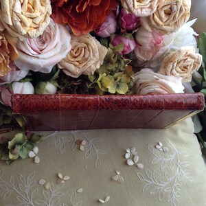 Peut inclure: Un journal reli&eacute; en cuir marron avec une couverture textur&eacute;e, semblable &agrave; du cuir de serpent. Le journal repose sur une surface en tissu blanc avec un motif floral.