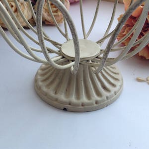 May include: White metal wire basket with a fluted base. The basket is designed to hold small items like fruit or bread.