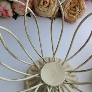 May include: White metal wire fruit bowl with a decorative base. The bowl is shaped like a flower with a circular base.