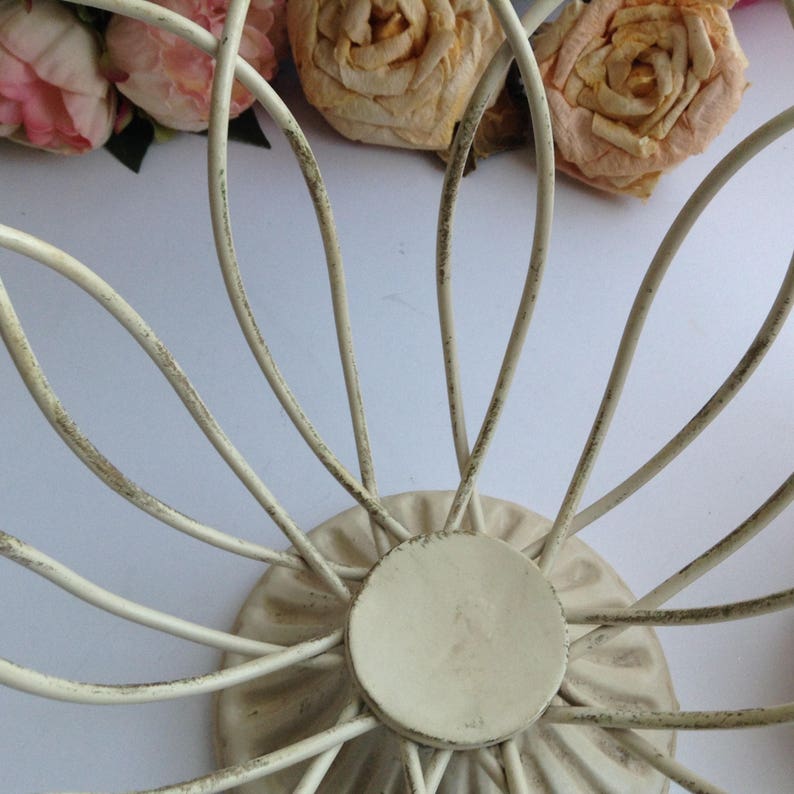 May include: White metal wire fruit bowl with a decorative base. The bowl is shaped like a flower with a circular base.