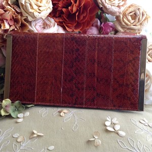 Peut inclure: Une pochette en cuir de serpent brun avec des accents en m&eacute;tal dor&eacute;. La pochette est de forme rectangulaire et a une surface lisse et textur&eacute;e.