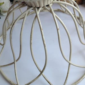 May include: White metal cake stand with a circular base and a decorative, scalloped top. The stand is made of wire and has a distressed finish.
