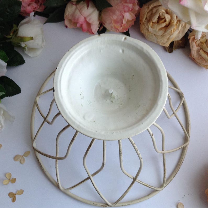 May include: White metal cake stand with a decorative, geometric design. The stand has a round base and a circular top.