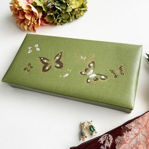 May include: A green rectangular jewellery box with a butterfly design. The box has a hinged lid and is made of a textured material.