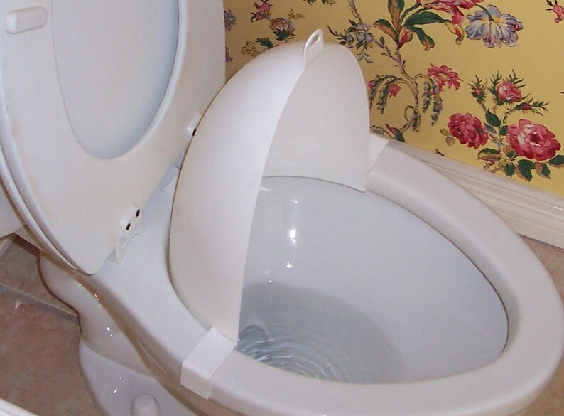 以下が含まれることがあります： 白い便器で蓋が開いており、白い飛沫ガードが付いています。 便器は花柄の壁紙を背景に設置されています。 便座も白です。
