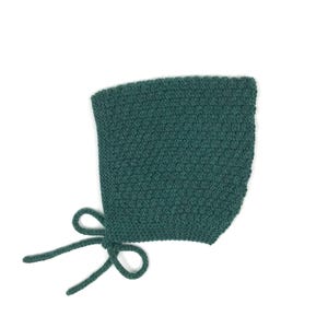 Peut inclure: Un bonnet de bébé tricoté vert sarcelle avec un motif texturé. Le bonnet a des liens de chaque côté pour le fixer. Le bonnet est fait de fil doux et est conçu pour garder la tête d'un bébé au chaud.